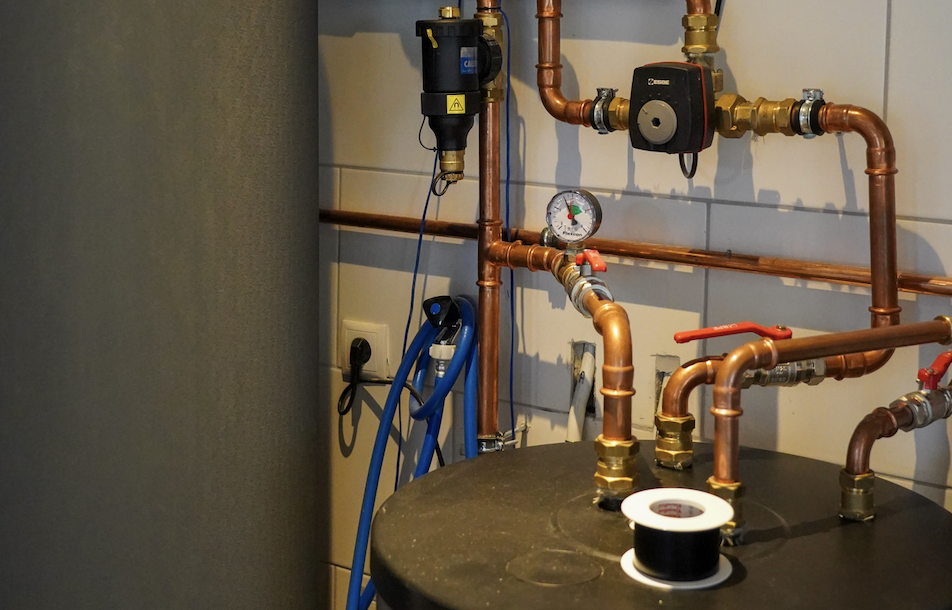 Cv-installatie met koperen leidingen, circulatiepomp, thermostaat en regelapparatuur op werkblad.
