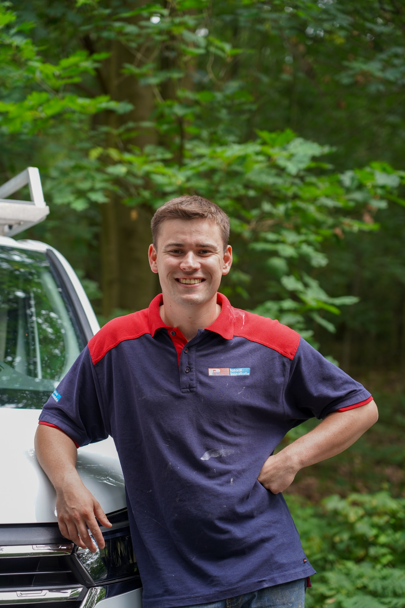 Medewerker van Polhuis in werkkleding leunt tegen servicewagen voor groene tuin, glimlachend naar camera.