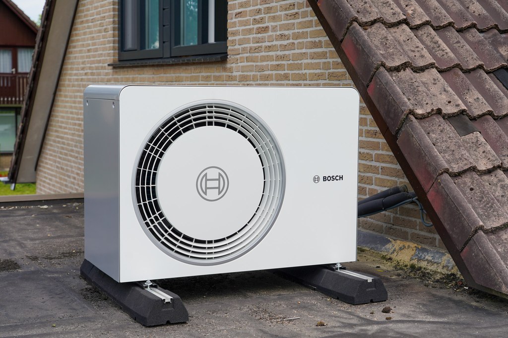 Bosch luchtbronwarmtepomp buiten opgesteld tegen bakstenen huismuur met dakpannen.